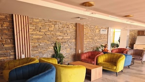 Un hall d’entrée moderne avec un mur en pierre, des fauteuils colorés et une table basse en bois.