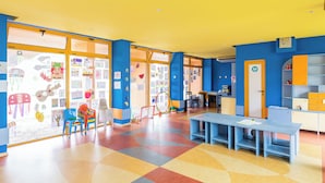Une salle de classe aux couleurs vives, avec des murs bleus, une grande fenêtre et un sol coloré.