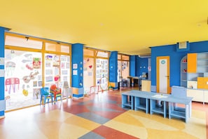 Une salle de classe aux couleurs vives, avec des murs bleus, une grande fenêtre et un sol coloré.