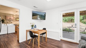 A modern kitchen with white appliances, a dining area with a wooden table and black chairs, and a large window with a view of a beach and mountains. - Long Term Stay Discount. Business, Couples and Families Welcome/Ground Floor (Bothell)