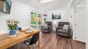 A modern living room with a wooden dining table, two grey armchairs, a grey sofa, a TV mounted on the wall, and a cityscape painting. - Long Term Stay Discount. Business, Couples and Families Welcome/Ground Floor (Bothell)