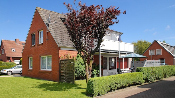 A residential house with a sloped roof, a visible chimney, and a well-maintained lawn. - Apartment "top right" - House Pamir (Neuharlingersiel)