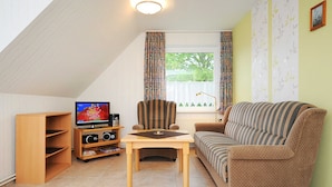 A living room with a television, a striped armchair, a sofa, and a wooden table. - Apartment "top right" - House Pamir (Neuharlingersiel)