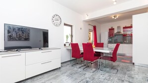 A modern kitchen with red chairs, a white dining table, and a large TV on a white cabinet. - Amazing apartment in Okrug Donji with WiFi (Okrug Donji)