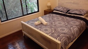 A bedroom with a bed, a window with a view of trees, a bedside table with a lamp, and a framed picture on the wall.