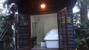 A small, enclosed outdoor structure with a single door leading inside. Inside, there is a white plastic container, a small table, and a chair.