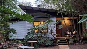 A modern house with a covered porch, surrounded by tropical plants and a gravel pathway.