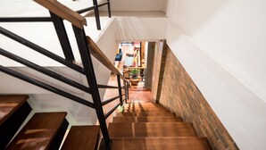 Eine Holztreppe mit schwarzen Geländern führt zu einem Raum mit einer Ziegelwand und einem Blumentopf.