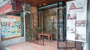 A hotel entrance with a tiled floor, a wooden bench, and a metal gate.