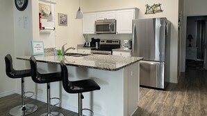 A modern kitchen with white cabinets, stainless steel appliances, a granite countertop, and black bar stools. - 1b/1b for 6 max4adults! Heated pools! Steps from the BEACH! Netflix! Playground! (Corpus Christi)