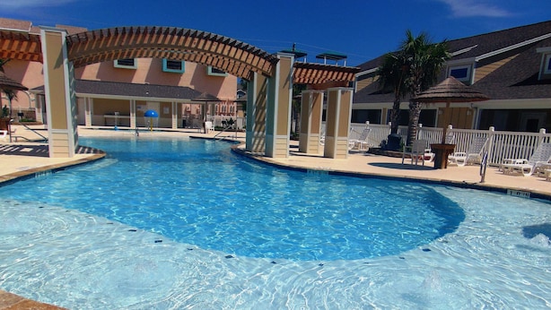 A swimming pool with a 10-foot entry, surrounded by lounge chairs and a covered seating area. - 1b/1b for 6 max4adults! Heated pools! Steps from the BEACH! Netflix! Playground! (Corpus Christi)