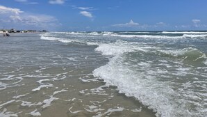 A beach with waves, a clear sky, and distant buildings. - 1b/1b for 6 max4adults! Heated pools! Steps from the BEACH! Netflix! Playground! (Corpus Christi)