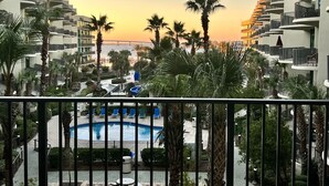 Een resort met een zwembad, palmbomen en uitzicht op een zonsondergang.