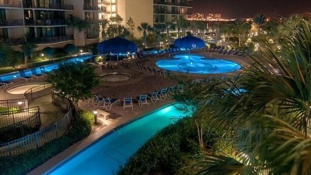 Een hotel met meerdere zwembaden, waaronder een groot centraal zwembad en kleinere baden, omringd door ligbedden en parasols.
