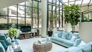 Een ruime binnenruimte met een groot raam, een zithoek, een televisie en verschillende planten.