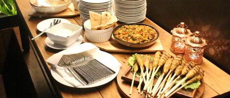 Una mesa de buffet con diversos platos, incluyendo carnes brochetas, cuencos de comida y platos apilados.