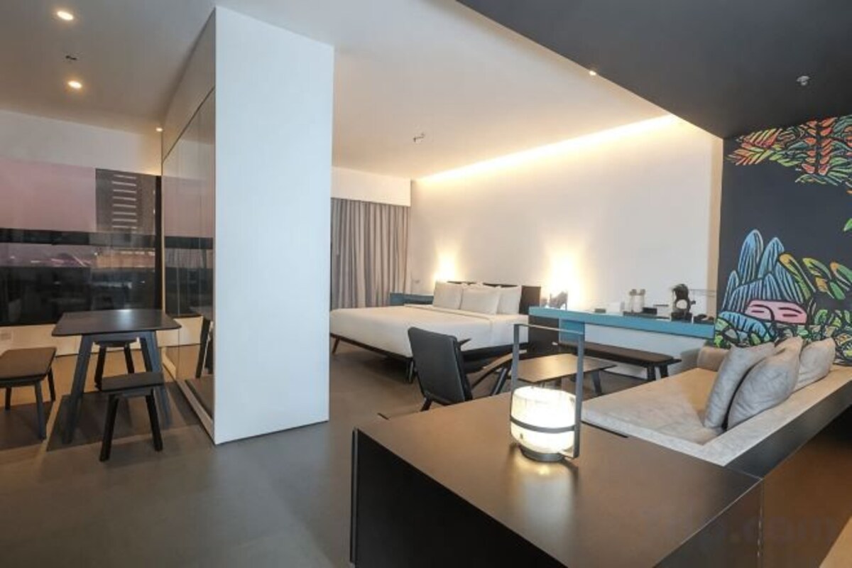 A modern hotel room with a bed, a desk, a sofa, and a dining table.