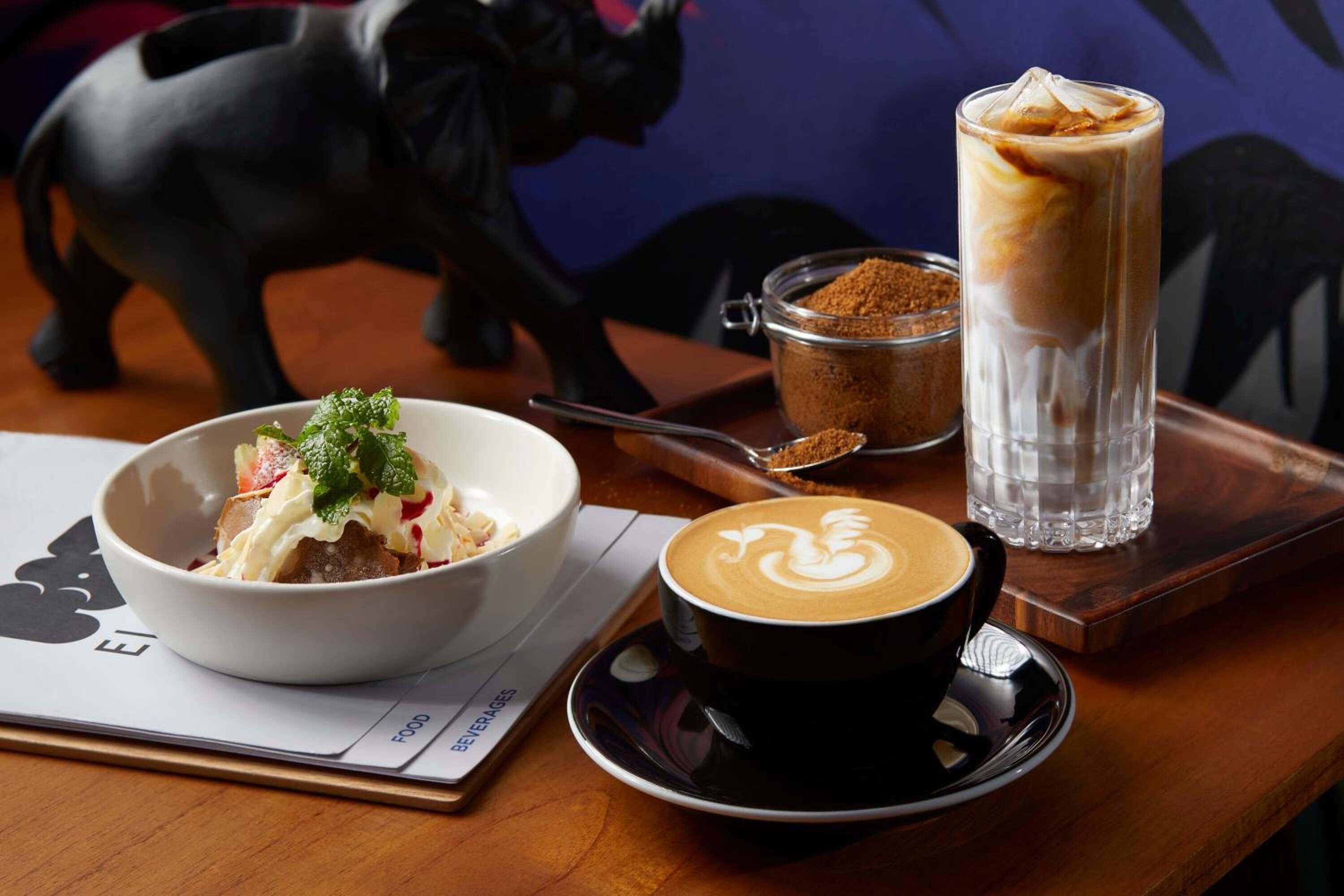 A table with a bowl of food, a cup of coffee, and a glass of iced coffee.