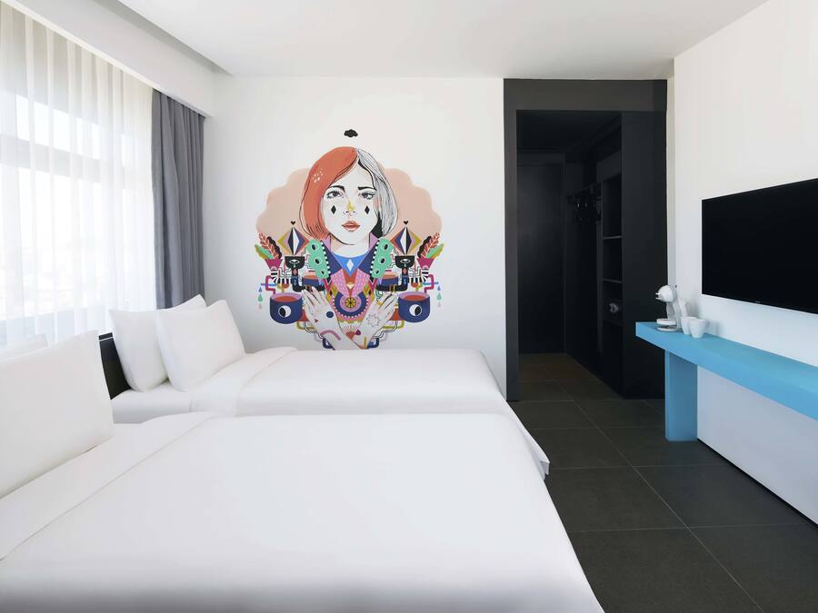A hotel room with a large bed, a TV mounted on the wall, and a colorful mural on the wall.