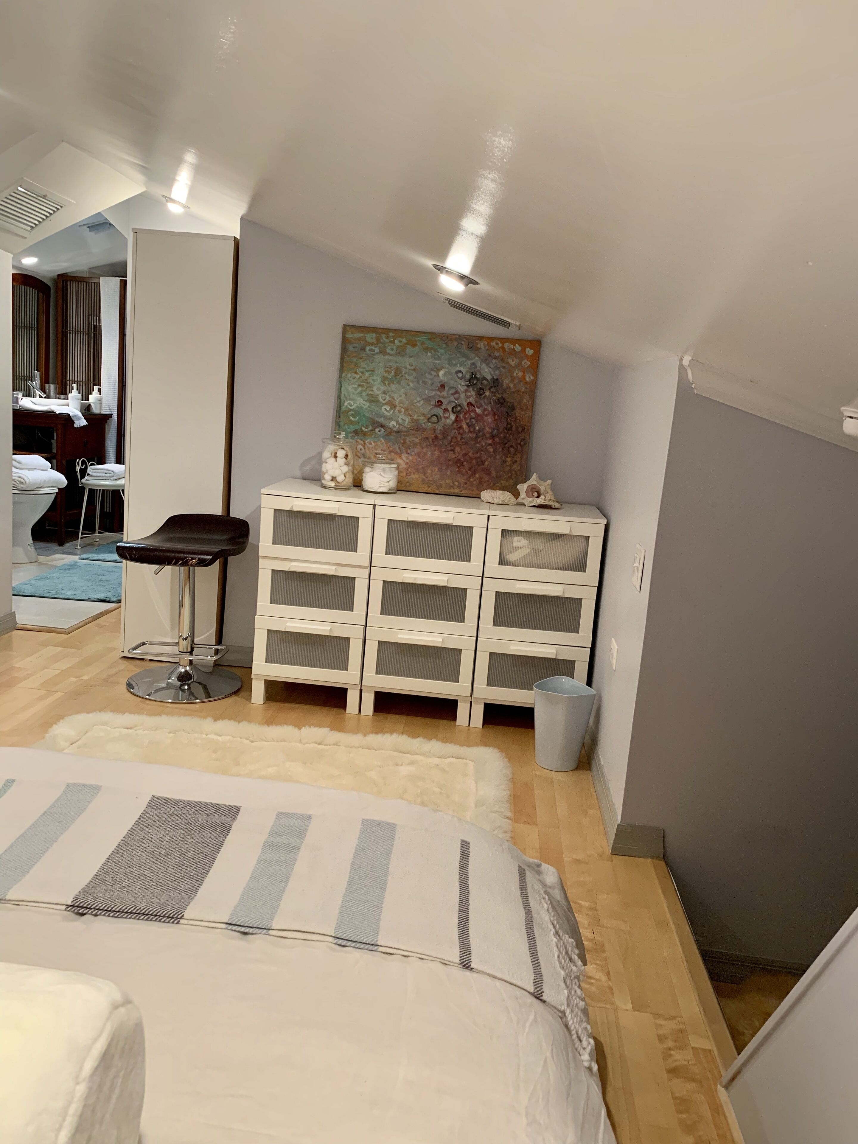 Une chambre à coucher avec un lit, une commode, un miroir et un tableau accroché au mur.