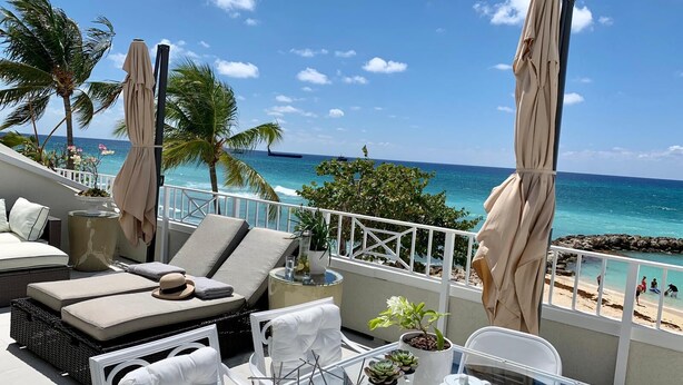 Ein Balkon mit Meerblick, ausgestattet mit einer Couch, Stühlen, einem Tisch mit Teekanne und Topfpflanzen.