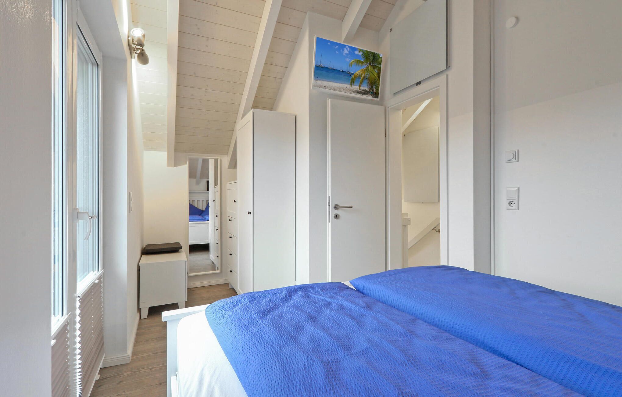 Ein Schlafzimmer mit Bett, Schrank, Schreibtisch und Meerblick durch ein Fenster.