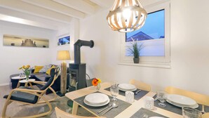 A modern living room with a dining area, a wood-burning stove, and a view of the sea through the window. - Beautiful home in Süssau/Ostsee (Süssau/Ostsee)