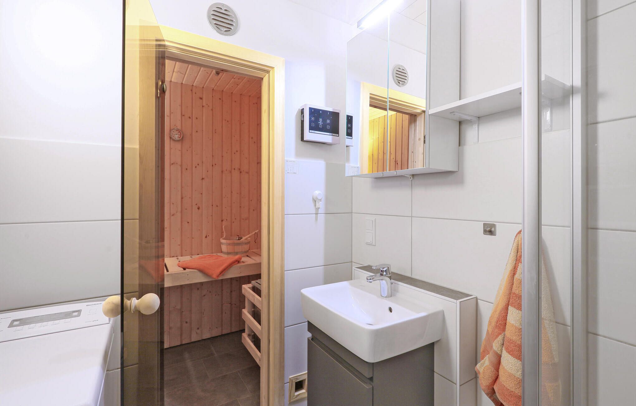 Une salle de bain moderne avec un sauna en bois, un lavabo blanc et une serviette accrochée au mur.