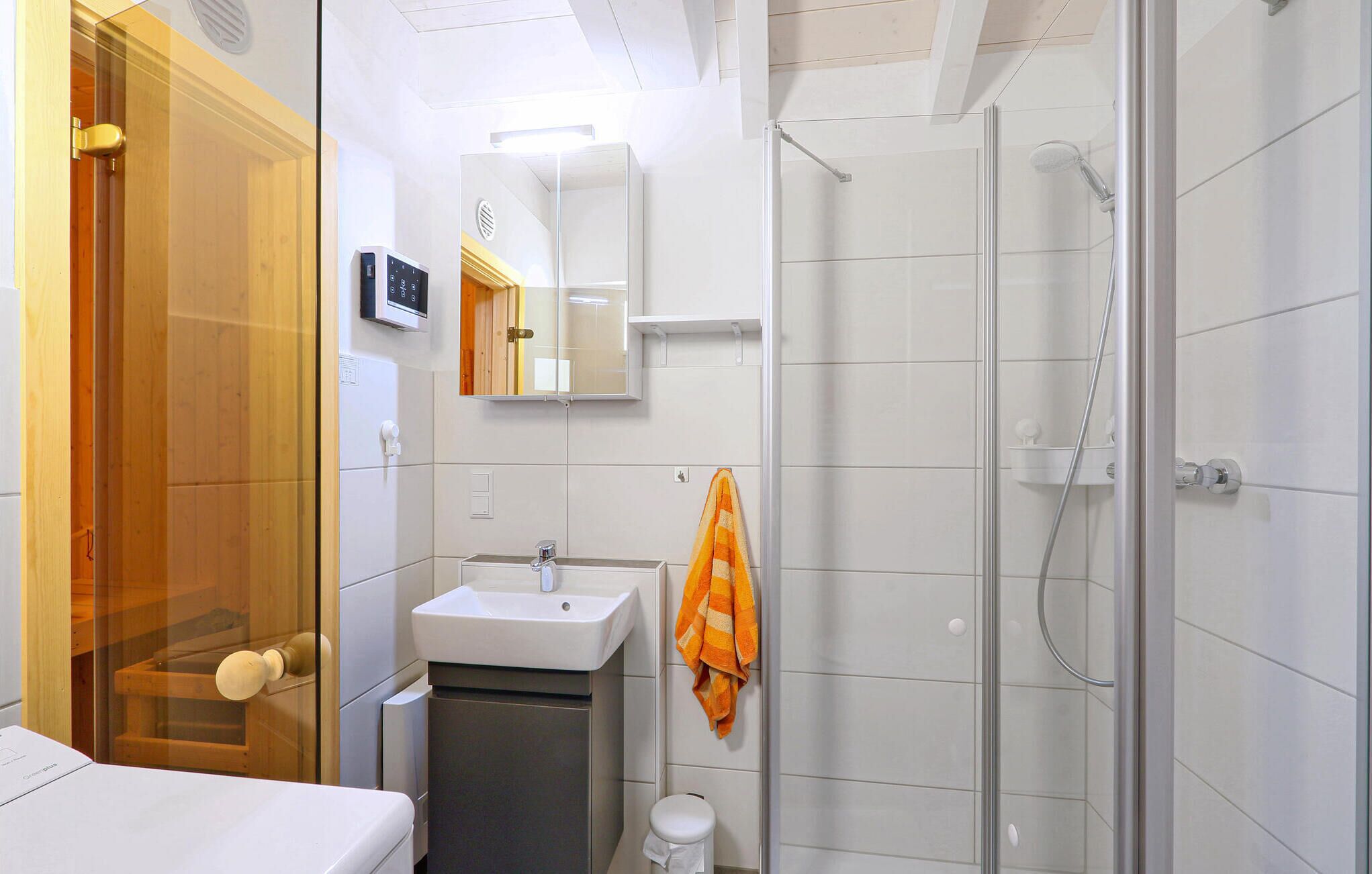 Ein modernes Badezimmer mit Duschkabine aus Glas, Waschbecken mit Spiegel darüber und einem Handtuch an der Wand.