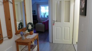 A hallway with a wooden bench, a potted plant, a mirror, and a door leading to a living room.