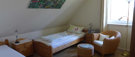 Une petite pièce agréable et confortable, avec un lit simple, une chaise, une table de chevet, une lampe et une fenêtre.