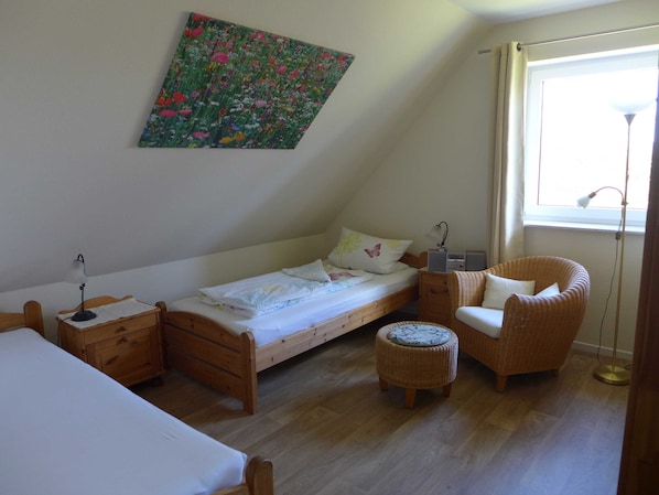 Une petite pièce agréable et confortable, avec un lit simple, une chaise, une table de chevet, une lampe et une fenêtre.