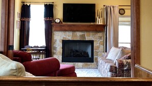 A living room with a stone fireplace, a television mounted above it, and a chandelier.