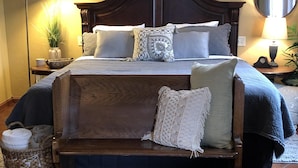 A neatly arranged bedroom with a large bed, a bedside lamp, a small table with a clock, and a mirror on the wall.