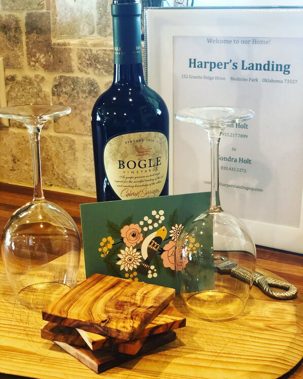 A wine bottle, two wine glasses, and a wooden coaster on a wooden table.