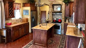 A spacious kitchen with wooden cabinets, a central island, a stone fireplace, and a chandelier.