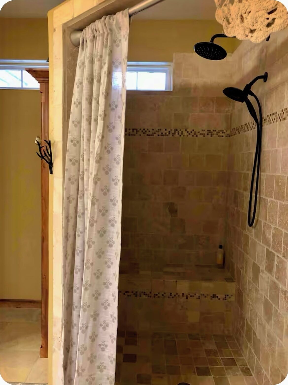 Zona de ducha con pared de azulejos, cabezal de ducha y cortina.