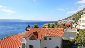 Eine Küstenstadt mit terrakottafarbenen Dächern, blauem Meer und einem Bergpanorama im Hintergrund.
