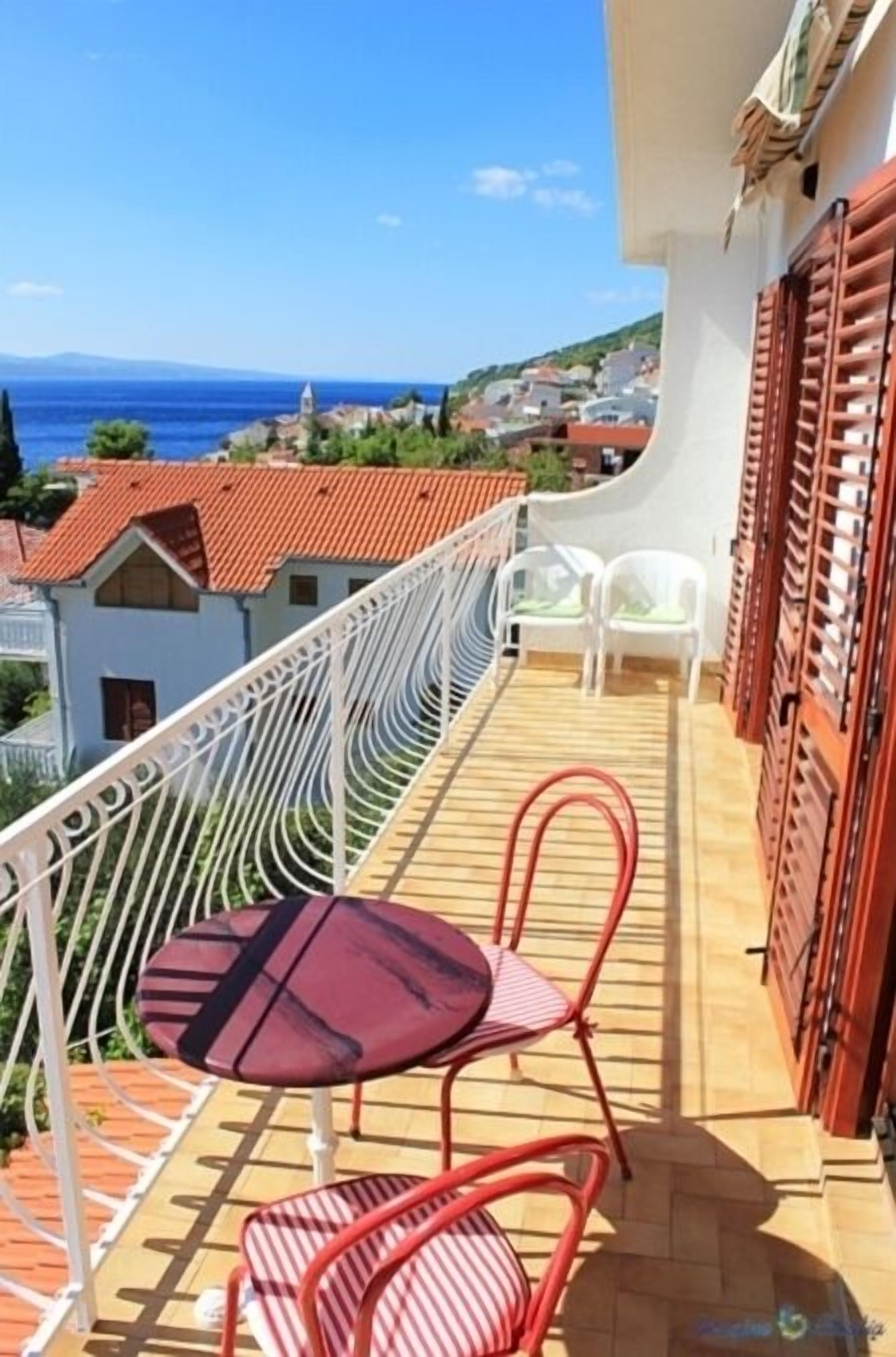 Ein Balkon mit Tisch und Stühlen mit Blick auf eine Küstenstadt und das Meer.