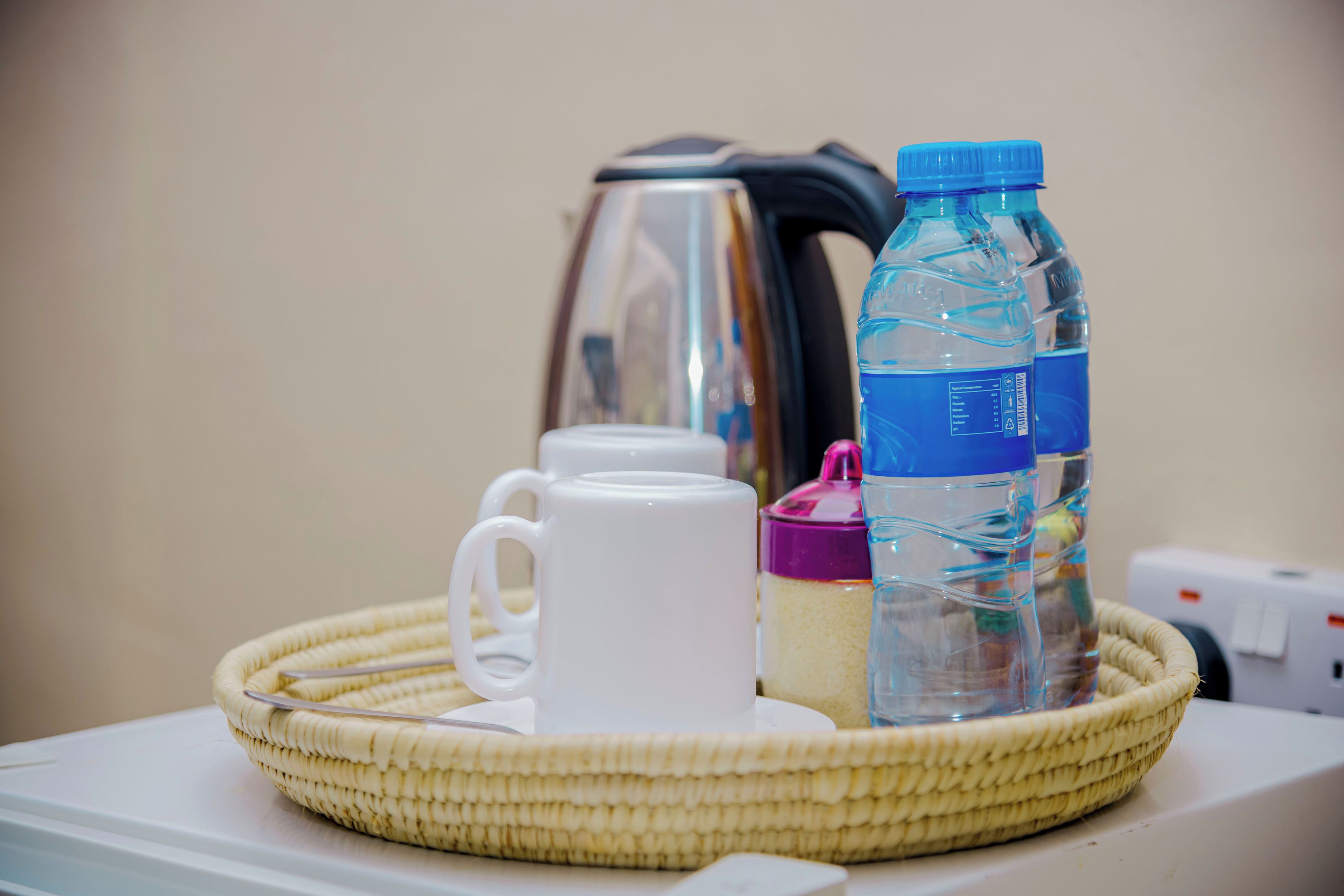 Un plateau avec une tasse blanche, une bouteille d’eau et une machine à café, le tout posé sur une table.