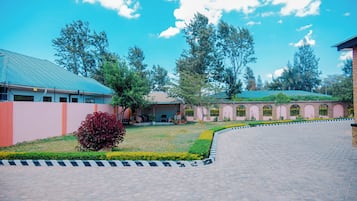 A courtyard with a paved walkway, a building with a green roof, and a brick structure with arched windows.