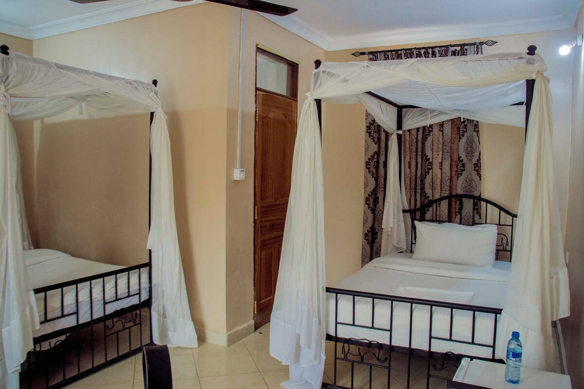 Dos llits individuals amb mosseres en una habitació amb parets beix i una porta de fusta.