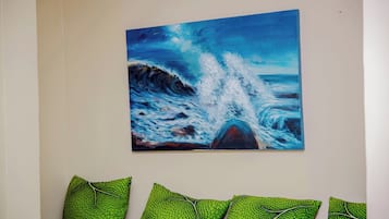 A painting of a wave on a wall, with a sofa and patterned cushions below.