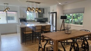 A modern kitchen with white cabinets, a central island with seating, and pendant lighting. - Contemporary Home In The Ventura Keys (Ventura)