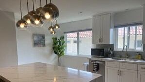 A modern kitchen with a marble island, white cabinets, a built-in microwave, and a large window with a view of the outside. - Contemporary Home In The Ventura Keys (Ventura)