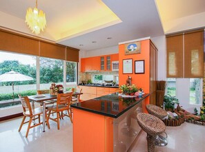 A modern kitchen with orange cabinets, a central island, and a dining area with wooden chairs. - Happiness Garden (Ji'an)