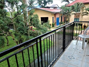 Un barrio residencial con una casa amarilla, un balcón con barandilla negra y piso de baldosas.