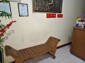 Un banco de madera en una habitación con suelo de baldosas, una placa en la pared y un pequeño armario con un letrero.