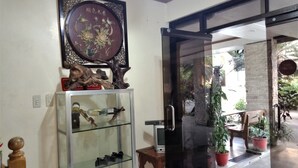 A room with a glass display cabinet containing various items, a television, and a door leading to an outdoor area with potted plants and a bench. - La Gracia Apartelle Tagaytay (Tagaytay)