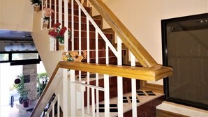 A staircase with white railings and a wooden handrail, leading to a landing with a large window and a television. - La Gracia Apartelle Tagaytay (Tagaytay)